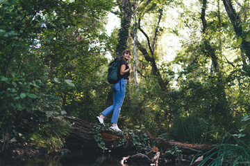 Trekking woman with backpack standing on tree trunk in forest