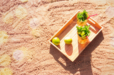 Two glasses of mojito cocktail with drinking straws on sand beach. Top view, copy space.
