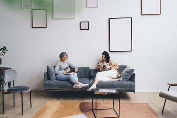 Busy mother and daughter sitting on sofa in living room