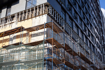 Extensive scaffolding providing platforms for work in progress on a new apartment block. Tall building under construction with scaffolds. Construction Site of New Building.