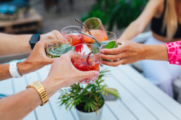 Group of friends toasting multicolored cocktails at the summer terrace