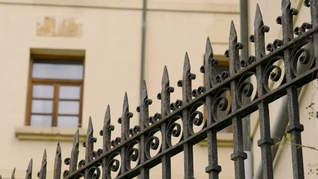Pointed spiked wrought iron fence made of forged metal against historical building with windows on a ancient house wall