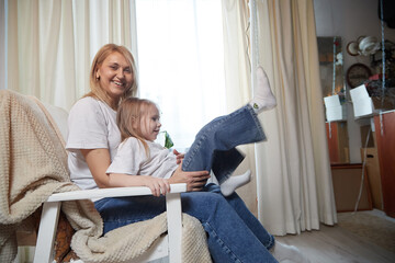 Happy loving family with mother and daughter in living room. Woman mom and small child girl playing and having convercation inside of the home