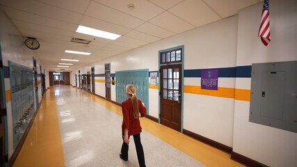 Wide angle view of back of teacher walking down empty school hallway with US American flag.