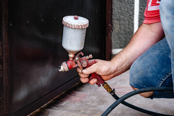 A painter painting a metal door with a spray gun.
