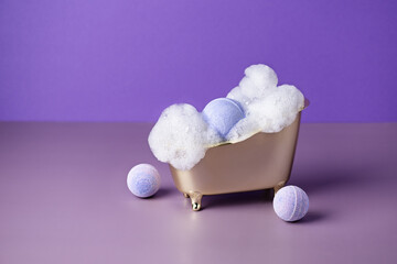 Salt bath bomb in a bathtub with soap suds on purple background. Creative idea of bath bombs for body care beauty spa treatment.