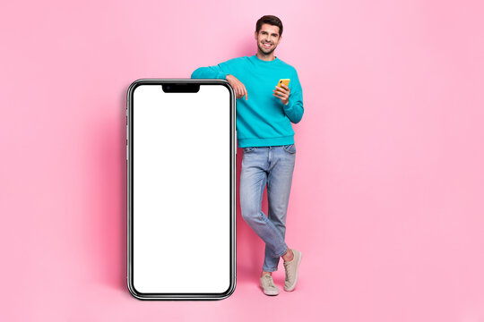 Full body photo of attractive young man hold device lean on blank banner dressed stylish blue clothes isolated on pink color background