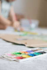 Naklejka premium Sweet little girl playing with paints. Child exploring his creativity by painting with watercolors in a home environment. Focus on foreground.