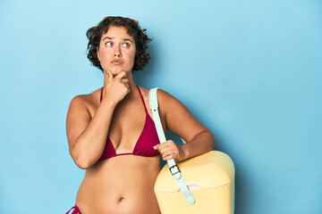 Young woman with cooler and summer look looking sideways with doubtful and skeptical expression.