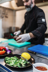 Handsome bearded professional chef works in restaurant kitchen. He prepares healthy delicious dish with fish and seafood.