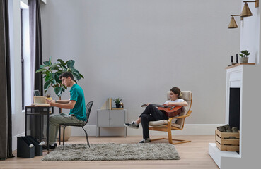 Two sibling brother and sister in the room, he is working and she is playing a guitar style.