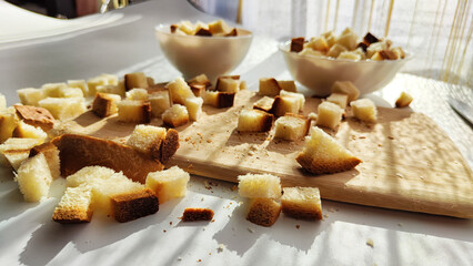 Homemade slices of diced dry white rye bread on cutting board and white plate. Crackers for food, healthy eating on table in sunny day, top view