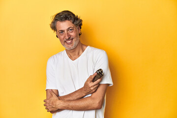 Man holding a razor, yellow studio background laughing and having fun.