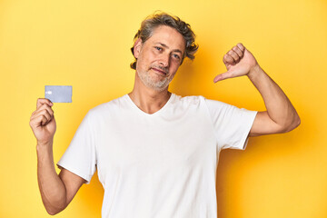 Man holding a credit card, yellow studio backdrop feels proud and self confident, example to follow.