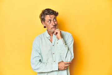 Middle-aged man posing on a yellow backdrop thinking and looking up, being reflective, contemplating, having a fantasy.