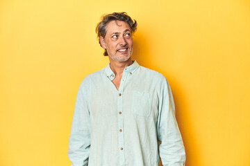 Middle-aged man posing on a yellow backdrop relaxed and happy laughing, neck stretched showing teeth.