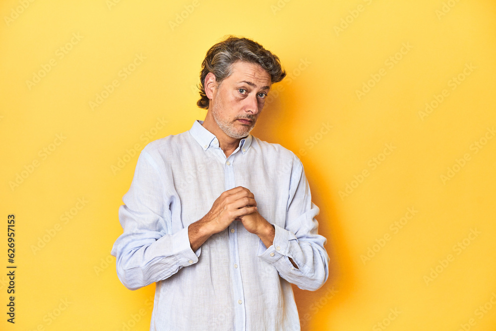 Wall mural Middle-aged man posing on a yellow backdrop scared and afraid.