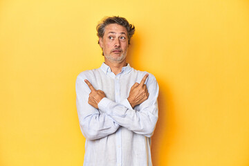 Middle-aged man posing on a yellow backdrop points sideways, is trying to choose between two...