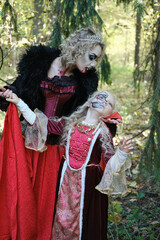 A woman in the form of a vampire or a sorceress poses in the forest with a girl in fairy-tale...