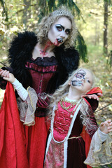A woman in the form of a vampire or a sorceress poses in the forest with a girl in fairy-tale...
