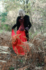 A woman in the form of a vampire or a witch in a medieval dress walks in the forest. Focus on plants