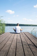 Man meditating near river, back view.