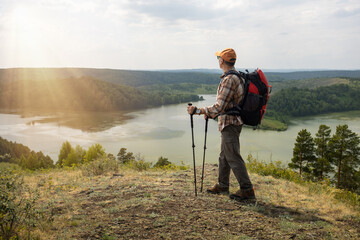  man hiker with backpack and walking poles is going in mountains at sunrise or sunset.