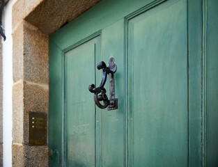 green wooden plank door with nails and decorative knocker, and with an intercom on the jamb