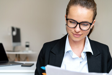 Businesswoman in a suit and glasses checks documents while working in the office.