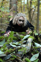 A woman in the form of a vampire or a witch crawls along the ground in a forest thicket. Focus on the branches lying on the ground
