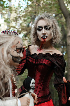 A woman in the form of a vampire or a sorceress and a girl in the form of a dead princess with a skeleton doll in their hands pose in the forest. Image for Halloween. Mother and daughter