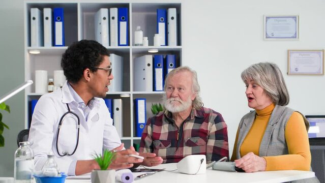 black doctor consults an elderly man and woman shows an x-ray while sitting in a medical office
