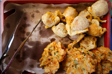 Piles of fried foods such as bakwan or fried vegetables are isolated in a container with a layer of oil paper. Bakwan is a traditional Indonesian food.