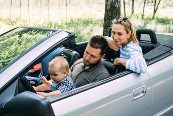 Mom, dad and little son in a convertible car. Summer family road trip to nature - obrazy, fototapety, plakaty