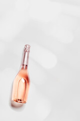 Top view sparkling rose wine with sun shadow and glare, romance beverage, bottle of champagne on light white gray background with copyspace. Festive Summer alcohol drink concept, pastel color