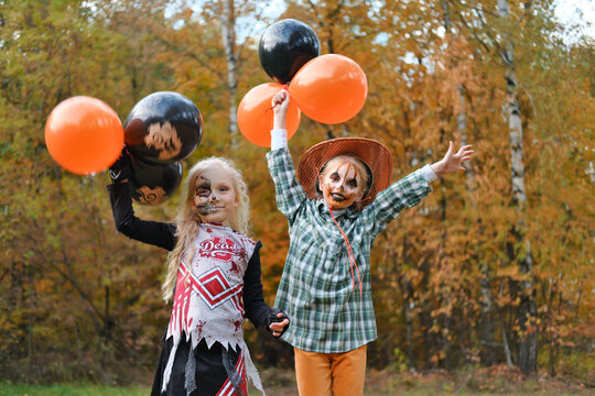 Two children girls girlfriends in Halloween costumes and makeup celebrate Halloween with black and orange balloons in their hands