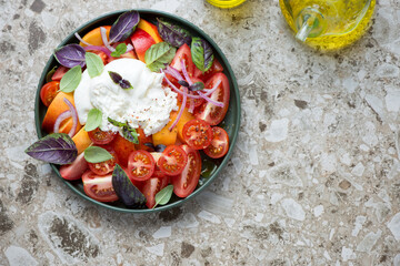 Plate of burrata, nectarines, tomato and basil salad, top view on a light-brown granite background, horizontal shot with space