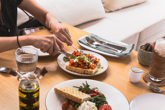 Female hands hold knife and fork cutting bruschetta appitizer on the plate.