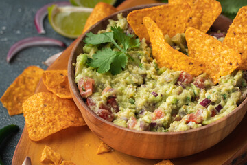 Wooden bowl of traditional Mexican guacamole with nachos on grey concrete background. Tortilla...
