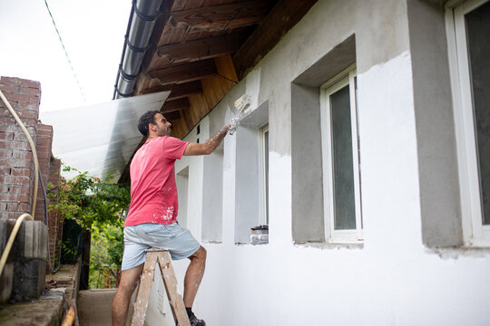 Standing man painting wall with roller brush in daylight