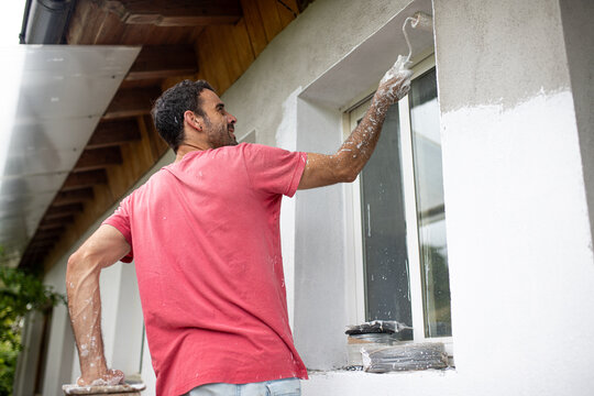 Standing man painting wall with roller brush in daylight