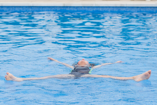 Unrecognizable kid floating in swimming pool water in daylight