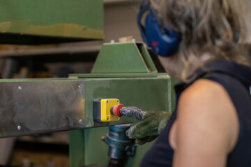 Anonymous woman in gloves pressing red button in factory
