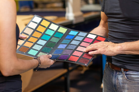 Crop man choosing colorful fabric samples with anonymous woman in daylight