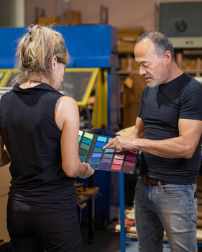 Serious middle aged man choosing colorful fabric samples with anonymous woman in daylight