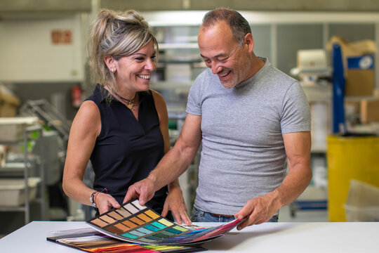 Happy middle aged man and adult woman examining colorful fabric samples in daylight