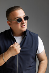 Obraz premium A cheerful young man model in a sleeveless regular solid jacket and a black sunglass posing in multiple different styles over white background with dimensions of width 5464 p and height 8192 p 
