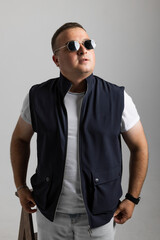 A cheerful young man model in a sleeveless regular solid jacket and a black sunglass posing in multiple different styles over white background with dimensions of width 5464 p and height 8192 p
