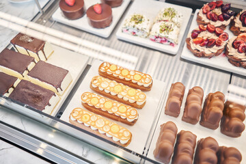 A variety of cakes covered with chocolate and decorated with pistachio mousse. A showcase in a pastry shop with delicious desserts with fresh berries and cream. Delicious pastries in the coffee shop.