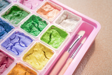 Dried colorful gouache in pink painting palette box with two pieces of white paint brush. Cracked water color and small brush.